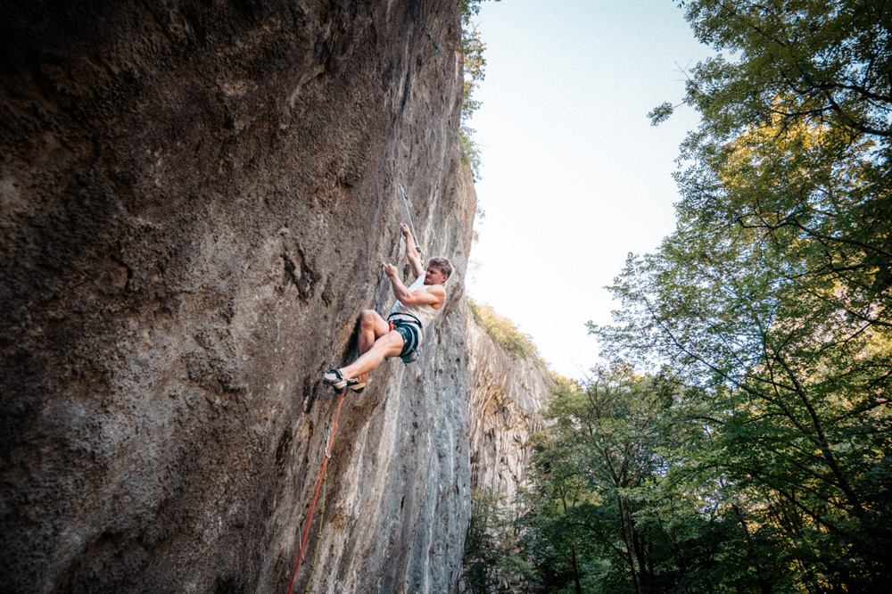 Grimpeur en tête dans une voie de falaise, bras tendu vers la dégaine suivante