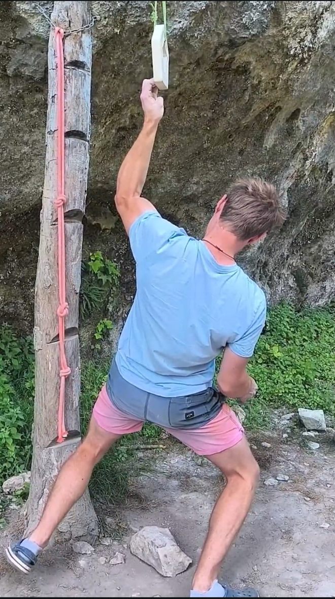 Puissance doigt semi-arqué en falaise : traction isométrique à un bras sur un bloc de bois suspendu, bras fléchi, épaule engagée, pied en appui