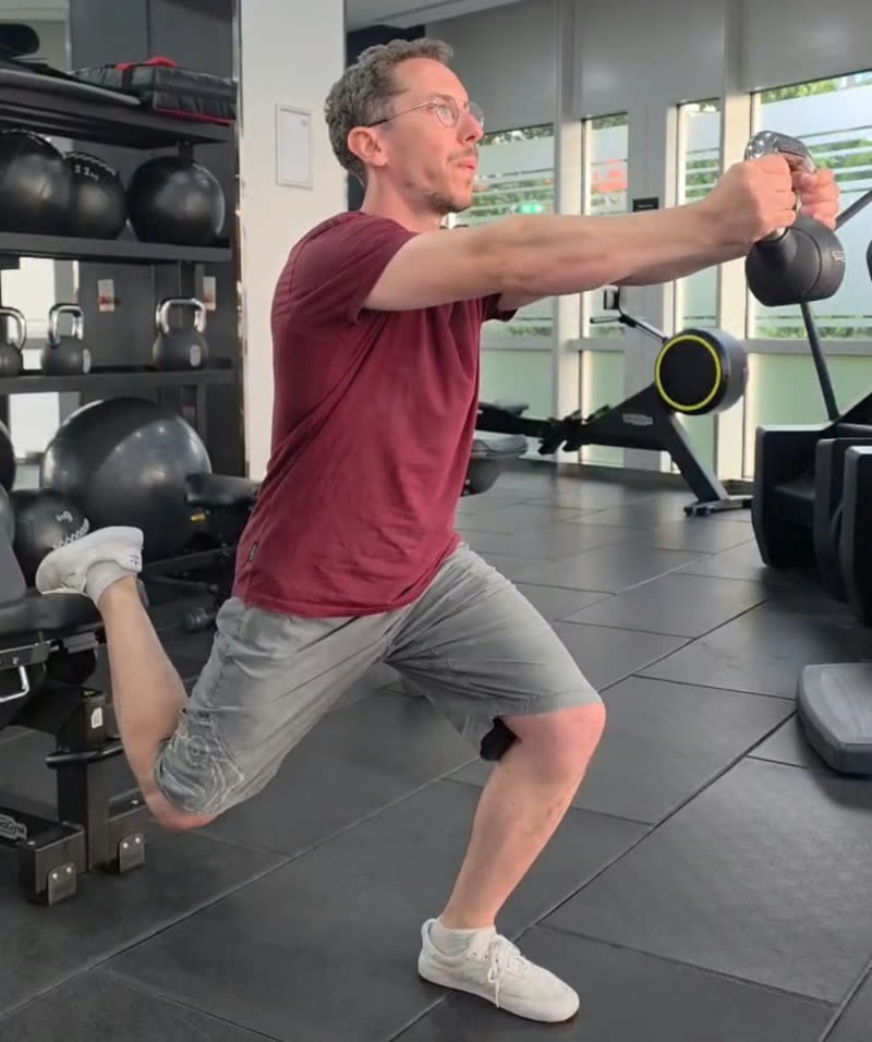 Rotation avec poids : position de fente, pied arrière surélevé sur un banc, kettlebell tenue à deux mains bras tendus devant